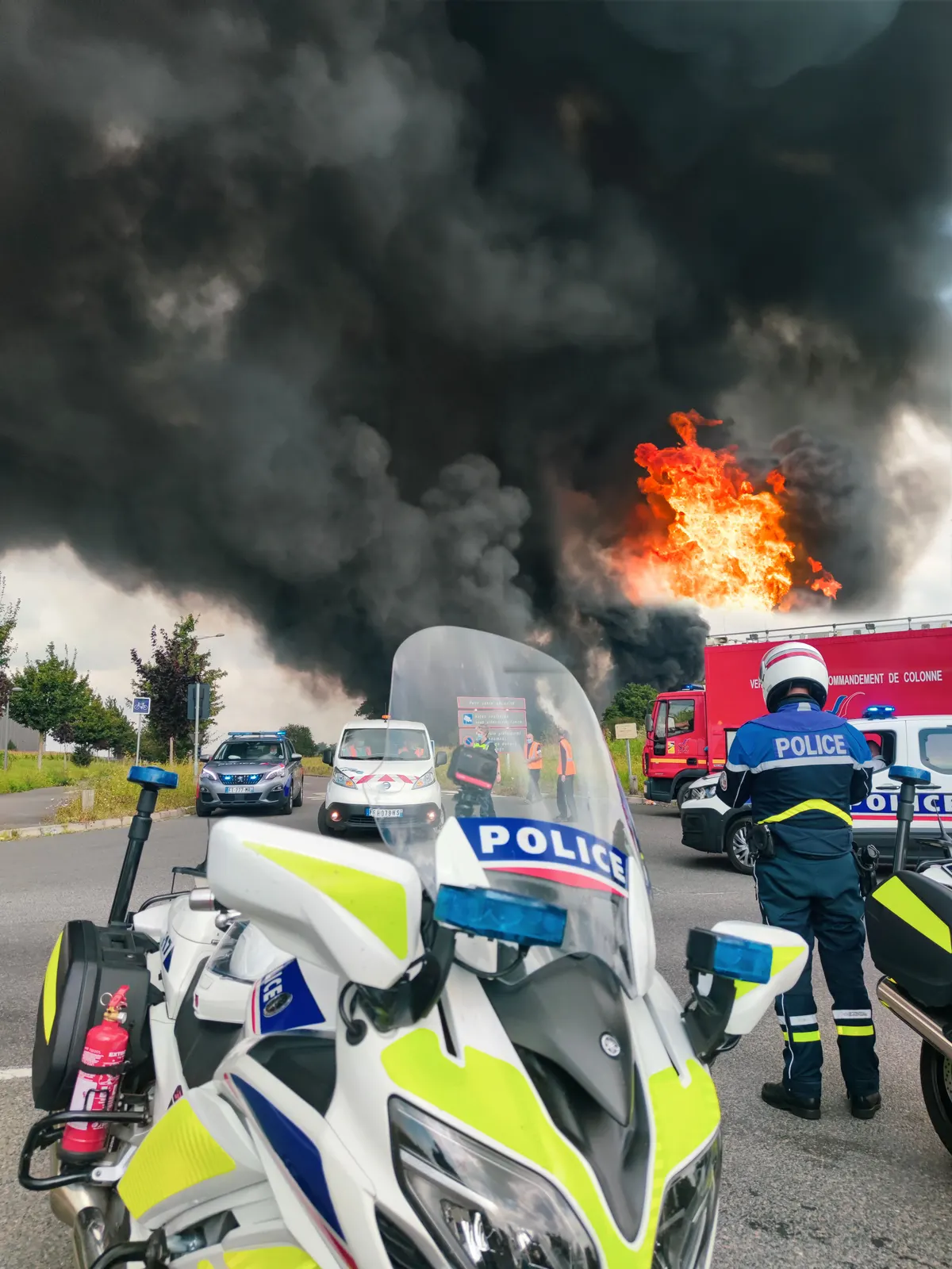 Motard de la police devant un incendie industriel, moyens de secours déployés sur la route